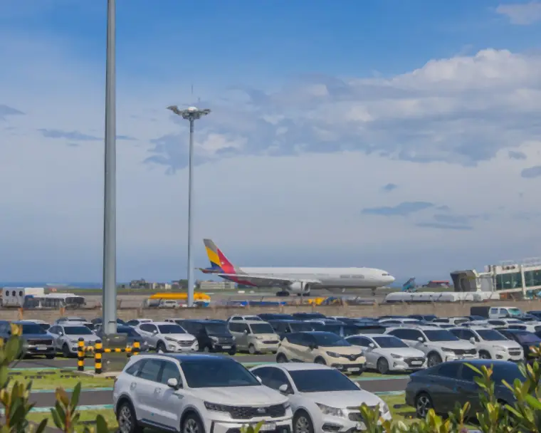 Cars parked at an airport car park with a plane taxiing behind