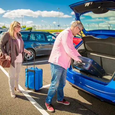 Travellers loading their suitcase into the car at an airport car park