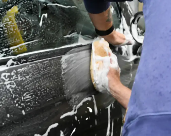 Hands washing a car door with a soapy sponge